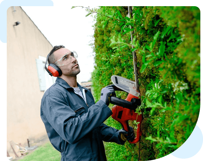 A man with ear muffs and goggles using an electric saw to cut the tree.